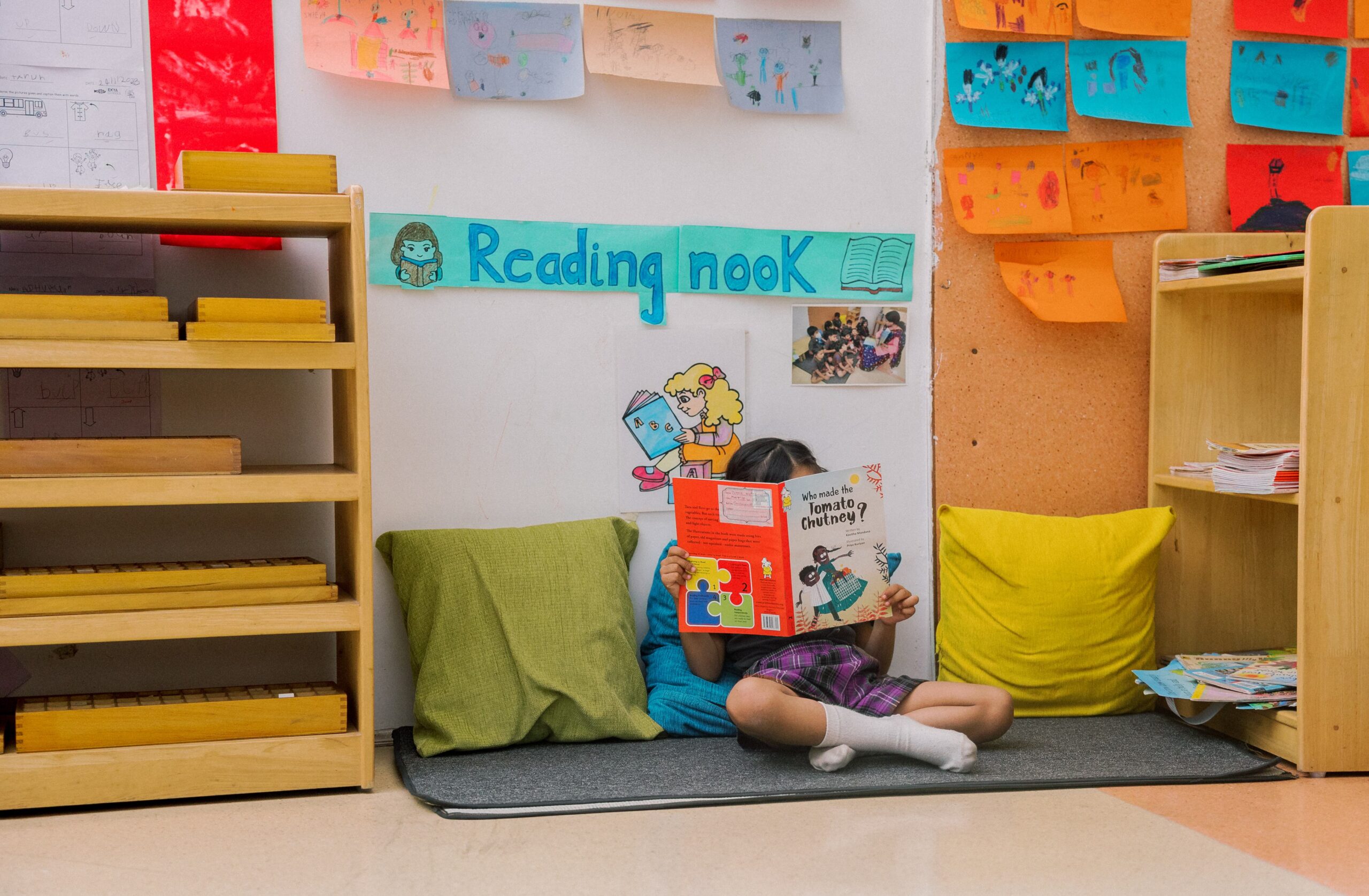 Reading nook at EKYA NAVA's purpose-based learning environment, featuring comfortable seating, wooden bookshelves, and colorful reading area design for students at international school in Panathur