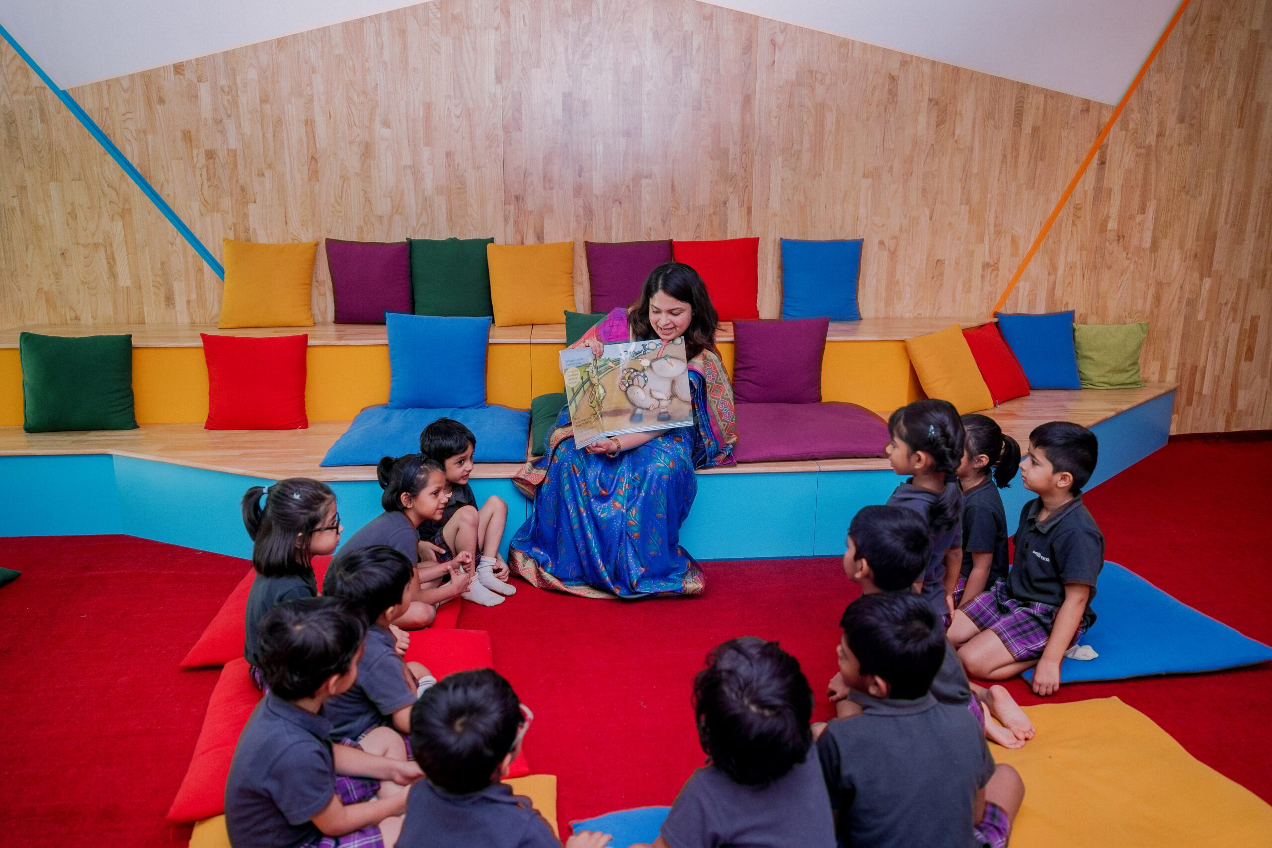 Teacher reading a storybook to young students at Ekya Nava's vibrant learning area.